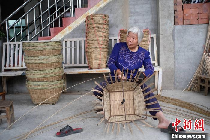 覃氏正在家门屋檐下编织竹筐。　刘俊聪 摄