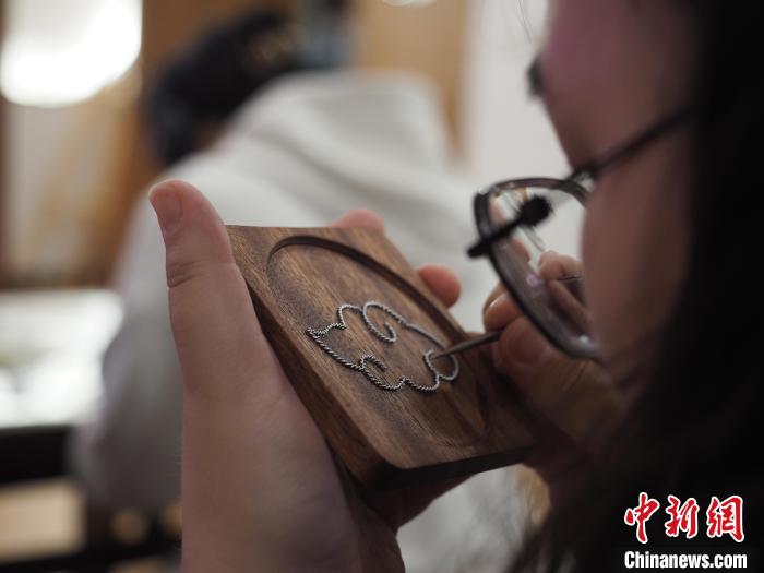 图为一名留学生在聚精会神地制作苗族银饰掐丝画杯垫。　李娇阳 摄