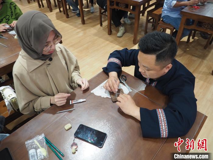 图为工作人员在指导一名留学生制作苗族银饰掐丝画杯垫。　李娇阳 摄